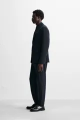 Pantalón de vestir azul marino, de corte slim fit, con bolsillos laterales y traseros. Se ajusta a la cintura con cinturón de cuero marrón.