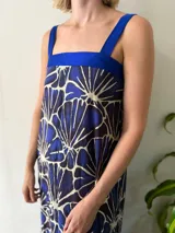 Vestido azul con estampado abstracto en blanco y azul oscuro. Presenta un escote cuadrado, tirantes anchos y un aplique de tafeta azul en el escote.