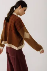 Cárdigan marrón con diseño de rombos en tonos rojizos y beige. Tiene cuello redondo, cierre frontal con botones y mangas largas con puños acanalados.