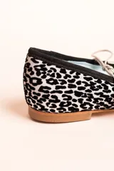 Bailarinas con estampado animal print en tonos blanco y negro, con cordones finos y borlas decorativas.