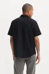 Camisa negra de manga corta con cuello clásico, cierre frontal con botones y bolsillo en el pecho.