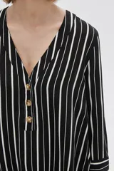 Camisa holgada de viscosa con estampado de rayas verticales en blanco y negro, cuello en V y mangas 3/4 con detalle de botones.