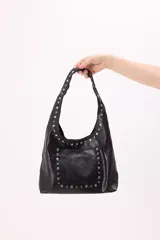 Bolso tipo hobo de símil cuero color negro, con tachas plateadas en el asa y en el bolsillo frontal.