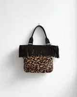 Cartera de cuero color mostaza con flecos estilo boho chic. Con cierre, interior forrado, dos bolsillos internos y portallave.