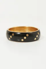 Pulsera rígida negra con puntos dorados.