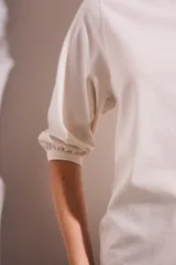 Remera color crema de algodón peinado, con mangas 3/4 abullonadas y corte ajustado al cuerpo.