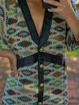 Vestido tipo abrigo con estampado geométrico en tonos azul, marrón y verde, con cuello en V, mangas abullonadas y cierre frontal con botones.