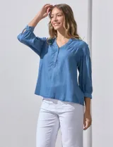 Blusa celeste de lyocell con cuello a la base y escote en V con apertura central y botones. Manga ¾ con puño y botón.