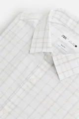 Camisa blanca con estampado de cuadros en tonos grises, corte regular fit, cuello italiano, manga larga con puños abotonados y cierre frontal con botones.