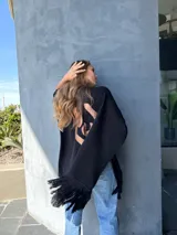 Ruana negra tejida en lana con aplique de cuero en la espalda y flecos en el ruedo.