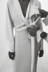 Vestido midi color crudo, con escote en V y mangas largas acampanadas. Cintura ajustable con lazos del mismo tejido.