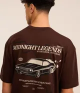 Remera marrón de corte relajado, cuello redondo y mangas cortas. Estampa frontal con un auto y la frase "Mindnight Legends Never Fade".