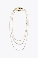 Set de tres collares dorados de diferentes largos. Uno es de eslabones metálicos con piezas circulares, otro es de cordón metálico con abalorios y perlas naturales, y el tercero es de cordón metálico liso.