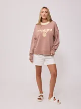 Sweater color ladrillo con cuello redondo en color crema. Estampado frontal con el texto 'Malibu Rusty' y un logo con forma de flor. Corte holgado.