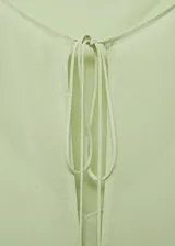 Blusa color verde claro de gasa semitransparente, con cuello redondo con lazos, mangas largas abullonadas con puños elásticos y diseño combinado.