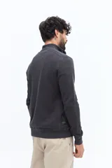 Buzo de algodón color verde musgo, con cuello alto y cierre frontal parcial. Presenta puños y cintura acanalados, y un pequeño logo bordado en el pecho.