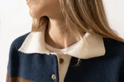 Sweater tejido de lana azul marino y marrón con cuello polo color crema y botones en el frente.
