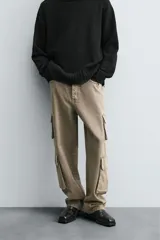 Pantalón de denim color beige, corte relaxed fit, con bolsillos laterales tipo cargo con solapa y cierre de botón. Cierre frontal con botón y cremallera.