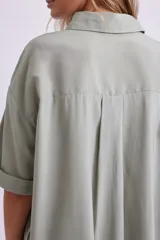 Camisa verde de corte holgado, con cuello clásico, cierre frontal con botones y mangas cortas con dobladillo.