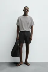 Bermuda negra regular fit confeccionada en tejido con mezcla de algodón y lino. Cintura elástica ajustable con cordón. Pliegues frontales. Bolsillos laterales y traseros de vivo. Cierre frontal con cremallera y botón.
