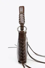 Bolso de hombro marrón de cuero sintético con dos bolsillos frontales con cremallera y tiras decorativas. El asa es trenzada y tiene herrajes metálicos.