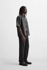 Sobrecamisa negra de manga corta confeccionada en tejido efecto piel, con cuello solapa, bolsillo frontal de parche y cierre frontal con botonadura oculta.