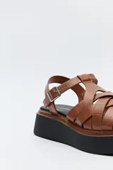 Sandalia negra con plataforma bicolor y capellada de tiras entrelazadas con textura símil reptil. Tiene hebilla metálica lateral para ajustar el calce y suela de goma.