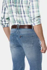 Pantalón de jean azul oscuro de corte recto y tiro medio. Incluye cinturón de cuero marrón y botas de gamuza marrón.