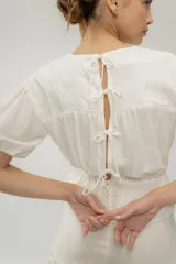 Blusa color chocolate con cuello redondo, mangas cortas abullonadas, detalle de flores bordadas en el frente y corte con volantes en la cintura.