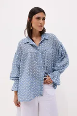 Camisa celeste a rayas verticales blancas, con cuello clásico, cierre frontal con botones y mangas largas abullonadas con puños elásticos.