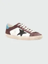 Zapatillas Golden Goose modelo Super Star, de cuero color marrón y blanco, con estrella negra en el lateral y detalles en celeste.
