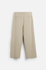 Pantalón color beige de corte ancho, con pliegues frontales, bolsillos laterales y traseros de doble vivo.