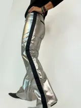 Pantalón plateado de cuero con corte sastrero, tiro medio alto, sin bolsillos y con una cinta lateral negra. Fabricado en Uruguay.