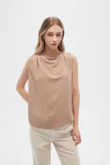 Blusa color beige de poliéster, sin mangas, con cuello asimétrico y detalle de drapeado en los hombros.