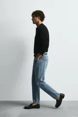 Jeans de denim de algodón, color negro lavado, con tiro medio, corte ajustado en cadera y muslos, y pierna que se estrecha hacia el tobillo. Presenta cinco bolsillos y cierre frontal con cremallera y botón.