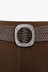 Bermuda color marrón chocolate de tiro alto con pinzas delanteras y cinturón trenzado. Bolsillos frontales. Cierre delantero con cremallera, botón interior y gancho.