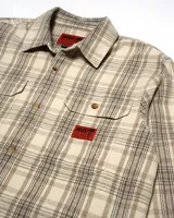 Camisa de franela a cuadros en tonos beige, gris y negro. Tiene cuello clásico, cierre con botones, dos bolsillos con solapa en el pecho y puños abotonados.