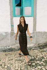 Vestido midi marrón de lino con cuello solapa, escote en pico y sin mangas. Presenta trabillas laterales con cinturón y cierre frontal con botones.