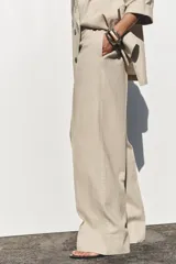 Pantalón color beige de lino, de tiro alto con cintura elástica, bolsillos laterales ocultos en costura y pernera ancha.