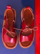 Sandalias rojas de cuero charol con cordones y suela marrón.