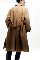 Abrigo color camel confeccionado en hilatura con lana. Tiene cuello solapa, manga larga, bolsillos delanteros ocultos en costura y cierre frontal cruzado con botones negros.
