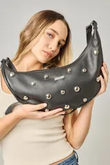 Cartera tipo bandolera de cuero sintético color celeste, con forma de media luna y tachas metálicas redondas plateadas en el frente. Posee correa ajustable y placa metálica con logo en la parte superior.