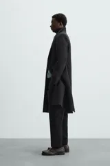 Abrigo negro regular fit confeccionado en paño con lana. Tiene cuello con solapas de muesca, manga larga, bolsillos de solapa en la cadera, bolsillo interior, abertura en el centro de la espalda y cierre frontal con botonadura.