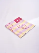 Pareo rectangular con rayas horizontales en tonos amarillo y lila, con estampado de conchas y texto "Guapa!".