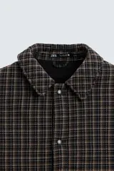 Sobrecamisa de hombre con corte relaxed fit, confeccionada en tejido de algodón acolchado con estampado a cuadros en tonos marrón, negro y beige. Tiene cuello solapa, manga larga con puños abotonados, bolsillo tipo parche en el pecho, aberturas laterales en el bajo y cierre frontal con botones a presión.