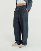 Pantalón de lino color gris gastado, con pinzas, silueta comba en piernas, bolsillos ojal en pierna izquierda y espalda. Largo hasta los tobillos y tiro medio.