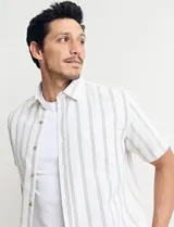 Camisa de manga corta a rayas verticales celestes y blancas, con cuello clásico y botones marrones.