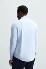 Camisa celeste a rayas verticales blancas, de corte recto, con cuello italiano abierto, mangas largas con puños abotonados y cierre frontal con botones.