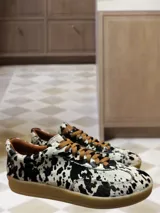 Zapatillas bajas con estampado animal print de vaca en blanco y negro, con cordones marrones y suela color caramelo.