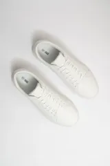 Zapatillas acordonadas blancas de cuero sintético, con suela plana de goma y cordones blancos.